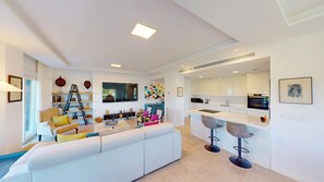 A modern living room with a white sofa, colorful cushions, a coffee table, and a bookshelf.