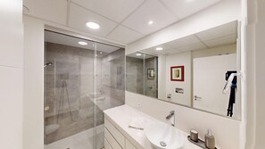 Ein modernes Badezimmer mit einer in Glas eingefassten Dusche, einem weißen Waschtisch mit Waschbecken und einem großen Spiegel.