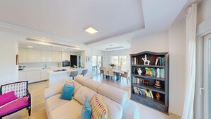 Una sala de estar moderna con sofá, estantería y comedor con mesa y sillas.