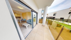 Un apartamento moderno con balcón, zona de comedor y cocina visible a través de la puerta de vidrio.