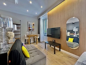 Un salon moderne comprenant un canapé, une table basse, un téléviseur et un coin repas avec des chaises et une table.