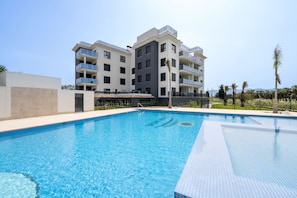 A swimming pool with a clear blue water surface, surrounded by a modern building with balconies and a flat roof.