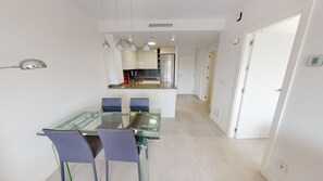 A modern kitchen with stainless steel appliances, a glass dining table, and purple chairs.