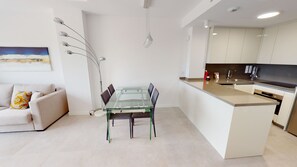 A modern apartment with a glass dining table, a sofa, a kitchen with a black countertop, and a pendant light. - Prímula by ON Travel (Oliva)
