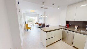 A modern kitchen with a central island, a dining area with a yellow chair, and a view of the outdoors.