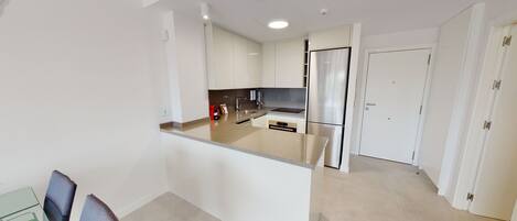 Una cocina moderna con armarios blancos, un refrigerador de acero inoxidable y un horno empotrado.