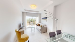 A modern living room with a sofa, a glass coffee table, a yellow armchair, a flat-screen TV, and a floor lamp. - Prímula by ON Travel (Oliva)
