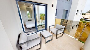 A balcony with a glass door leading to a room, two chairs, and a small table.