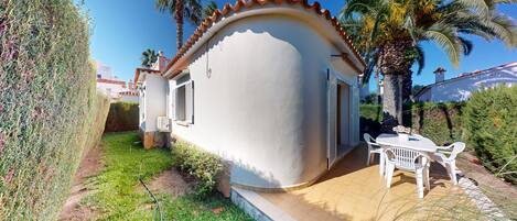 A small house with a white exterior, a tiled roof, and a patio with a table and chairs.