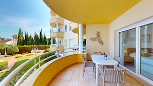 A balcony with a table and chairs, a view of the garden, and a building with balconies.