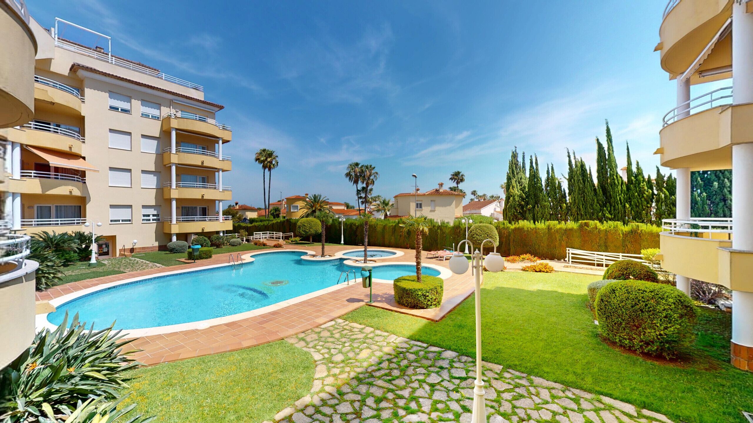A swimming pool surrounded by well-maintained lawns and a multi-story building with balconies.