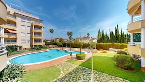 A swimming pool surrounded by well-maintained lawns and a multi-story building with balconies.