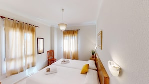 Ein Hotelzimmer mit zwei Betten, einem Holzstuhl, einem Nachttisch mit Lampe und einem gerahmten Bild an der Wand.