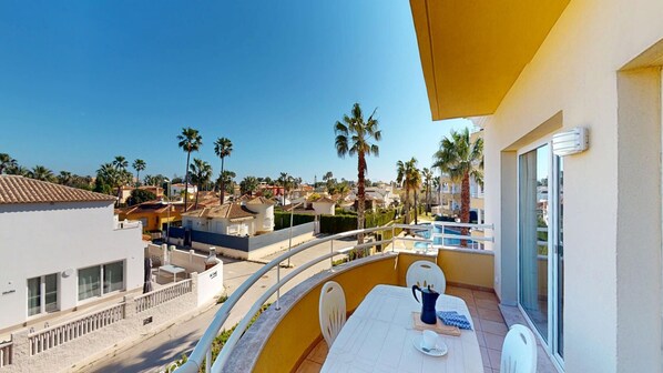 A balcony with a table and chairs, overlooking a residential area with palm trees and houses.