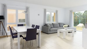 A modern living room with a dining area, grey sofa, white coffee table, and a balcony with a view of palm trees. - Seraph by ON Travel (Oliva)