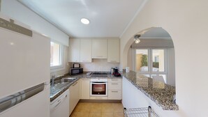 A compact kitchen with white cabinets, a granite countertop, a built-in oven, and a dishwasher. - Gloire by ON Travel (Oliva)
