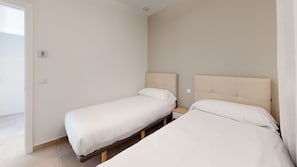 Une chambre avec deux lits simples, une table de chevet et un thermostat fixé au mur.