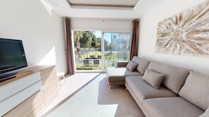 A modern living room with a flat-screen TV, a sofa, and a large window with a view of a residential area.