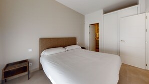 A bedroom with a large bed, a wooden headboard, a small bedside table, and a wardrobe.