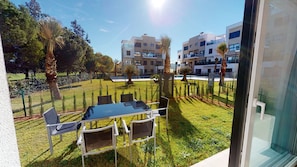 Un balcon avec une table et des chaises, donnant sur un espace verdoyant avec des arbres et un bâtiment en arrière-plan.