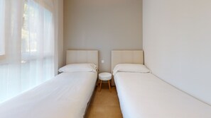 A room with two single beds, a small round table, and a window with sheer curtains.