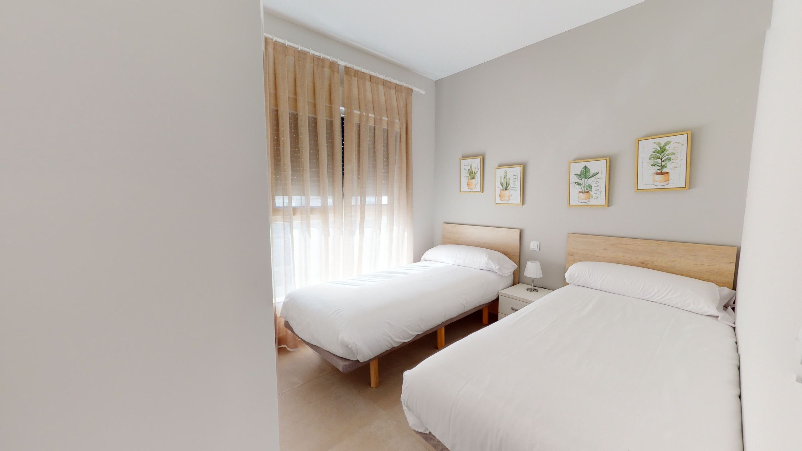 Une chambre avec deux lits, une table de chevet avec une lampe et une fenêtre avec des rideaux légers.