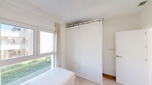 A bedroom with a bed, a wardrobe, and a window with a view of a building and greenery.