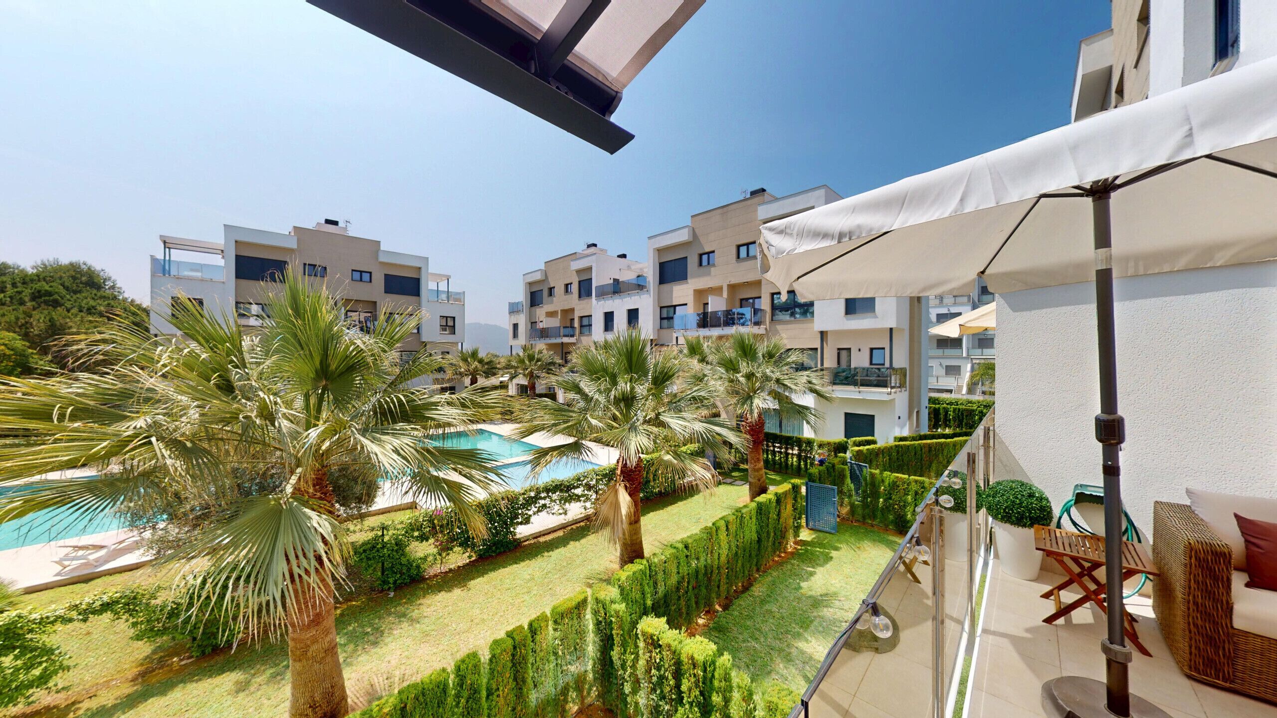 A modern hotel with a pool, palm trees, and a well-maintained garden.
