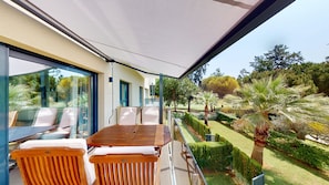 Eine moderne Terrassenanlage mit Holztisch und -stühlen, einem Glasgeländer und Blick auf einen gepflegten Garten mit verschiedenen Pflanzen und Bäumen.