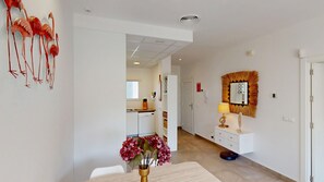 A modern kitchen with white cabinets, a dining area with a white table and chairs, and a hallway with a white door and a mirror with a decorative frame.