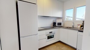 Une cuisine moderne avec des meubles blancs, un four encastré, un four à micro-ondes et une machine à café.