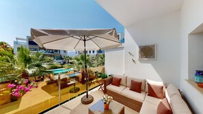 A balcony with a sofa, a table with a vase of flowers, and a pool in the background.