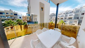 Ein moderner Balkon mit Glasgeländer, weißen Kunststoffstühlen und einem Tisch.