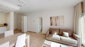 A modern living room with a sofa, a dining table, and a kitchen area.