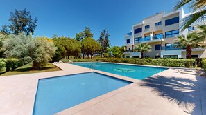 Una piscina con superficie de agua azul cristalina, rodeada por un suelo empedrado. Se observan sillas de descanso y una palmera.