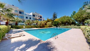 A swimming pool with a logo, surrounded by a tiled deck, palm trees, and a building in the background.