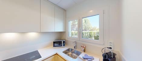 A modern kitchen with a built-in microwave, stainless steel sink, and a window with a view of trees.