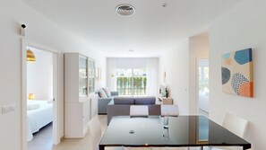 Una habitación moderna y bien iluminada con una mesa de comedor de vidrio, un sofá y una cama.