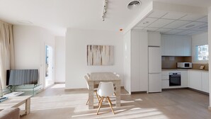 A modern living room with a dining table, white chairs, a flat-screen TV, and a kitchen area with white cabinets and appliances. - Palmetto by ON Travel (Oliva)