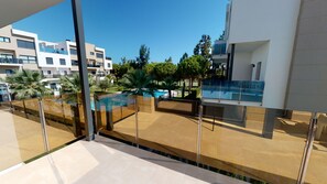A modern building with a glass balcony overlooking a swimming pool and greenery.