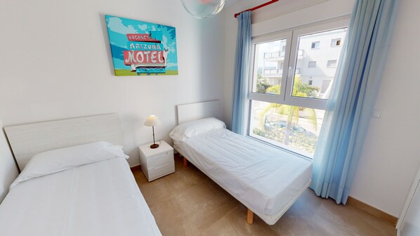 A bedroom with two beds, a nightstand, a lamp, a window with curtains, and a wall poster advertising a vacancy at an Arizona motel.