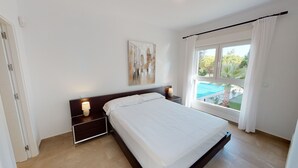 Ein Schlafzimmer mit einem Bett, Nachttischlampen, einem Gemälde und einem Fenster mit Blick auf einen Swimmingpool.