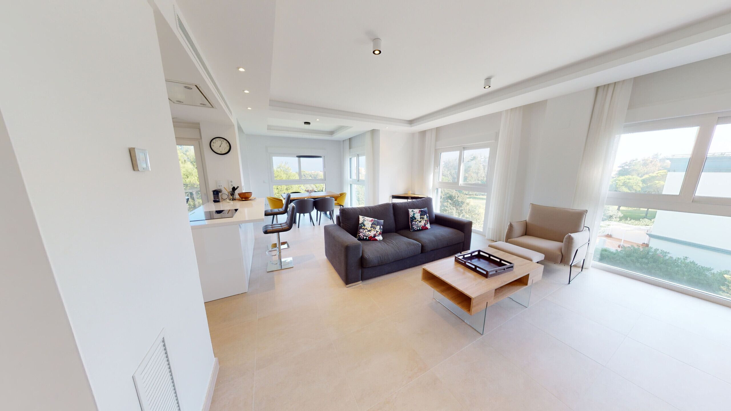 A modern living room with a sofa, coffee table, and a dining area with chairs and a table.