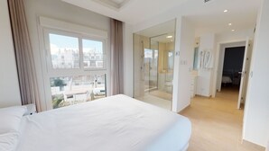 A modern hotel room with a large bed, a glass shower enclosure, and a view of the cityscape. - Forsitia by ON Travel (Oliva)