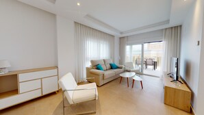A modern hotel room with a sofa, a chair, a coffee table, a TV, and a balcony with outdoor seating. - Forsitia by ON Travel (Oliva)