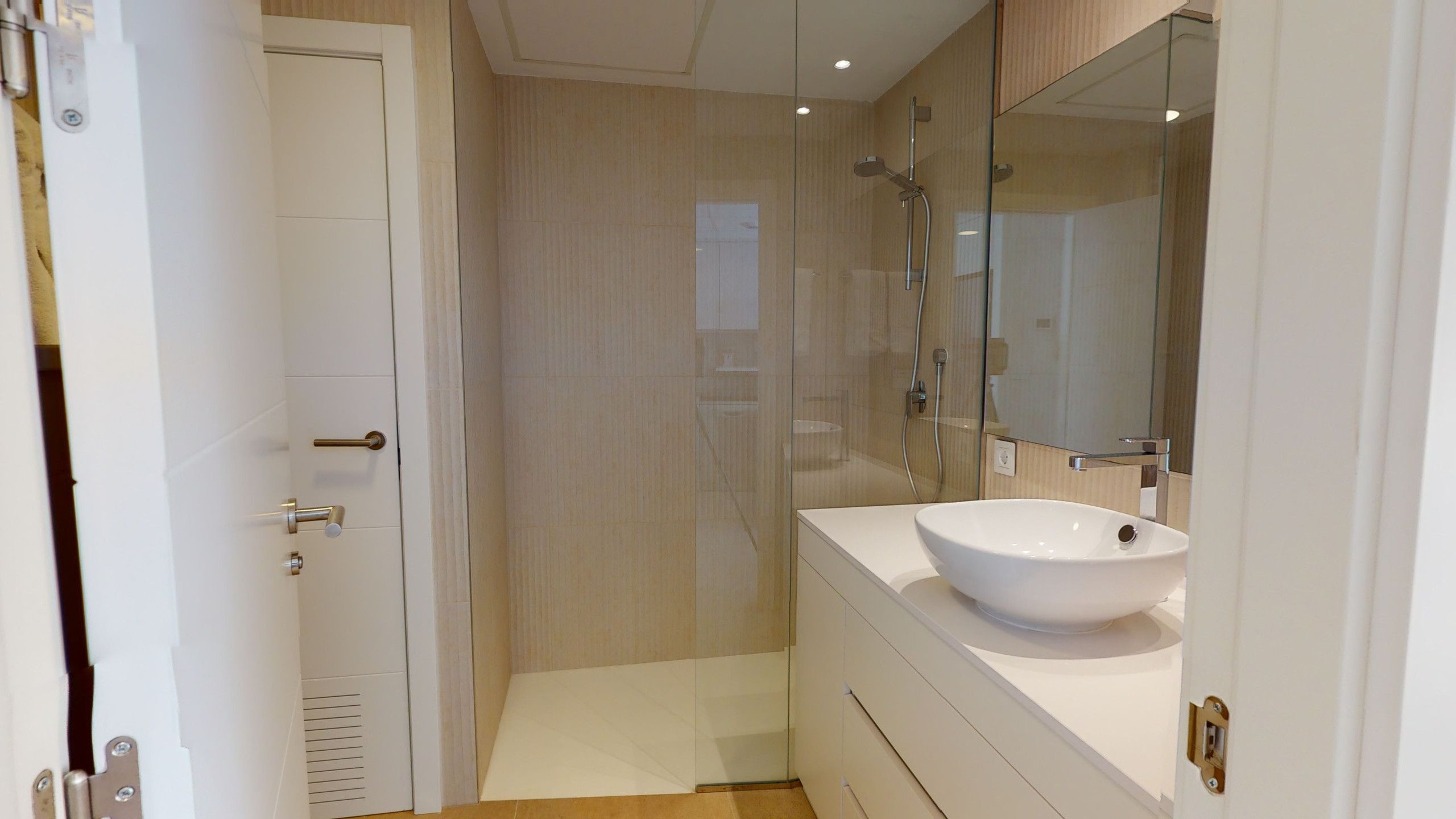 Ein modernes Badezimmer mit einem weißen Waschbecken, einer Duschkabine aus Glas und einer Tür mit einer Metallgriff.