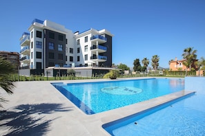 A modern building with balconies, a swimming pool, and palm trees.