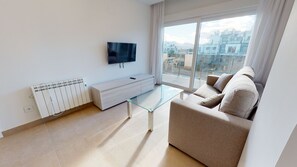 A modern living room with a sofa, a glass coffee table, a TV mounted on the wall, and a radiator.