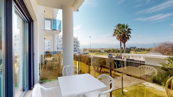 A balcony with a table and chairs, overlooking a residential area with palm trees and a clear sky. - Greenery by ON Travel (Oliva)