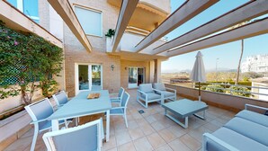 Een terras buiten met een tafel, stoelen, een pergola en uitzicht op de stad.